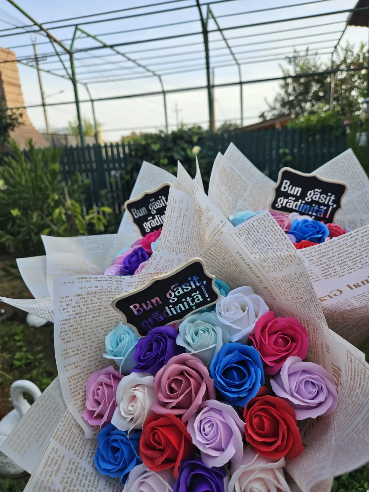 Buchet din 19 trandafiri de săpun multicolori în ambalaj cu imprimeu de ziar, cu toppere „Bun găsit grădiniță” și „clasa I”